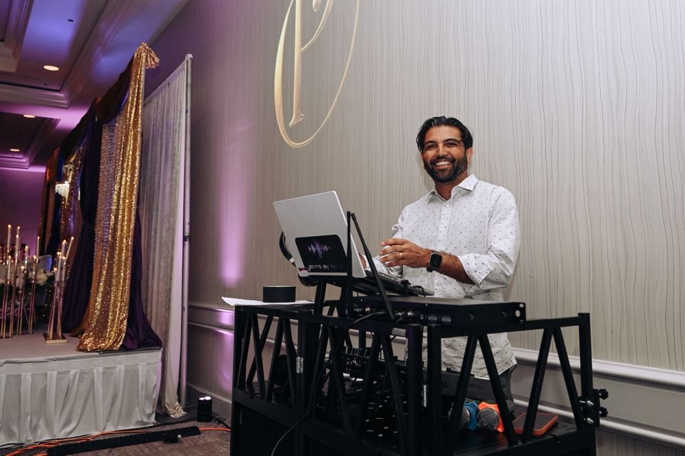 DJ RKADE smiling behind his DJ booth at a wedding reception